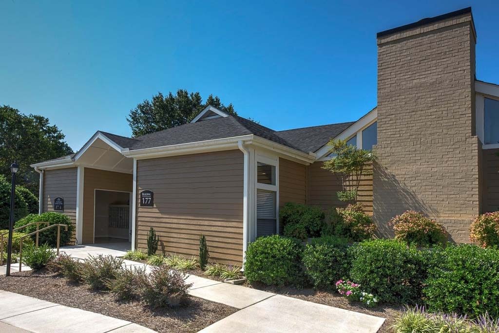 A house with a brown siding and a grey roof with a small garden in front at Fox Hollow Apartment Homes, High Point, NC, 27265