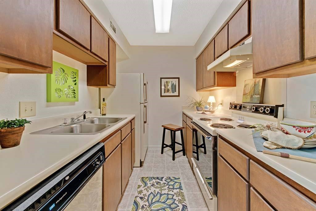 A kitchen with wooden cabinets and a black dishwasher at Fox Hollow Apartment Homes, High Point, NC
