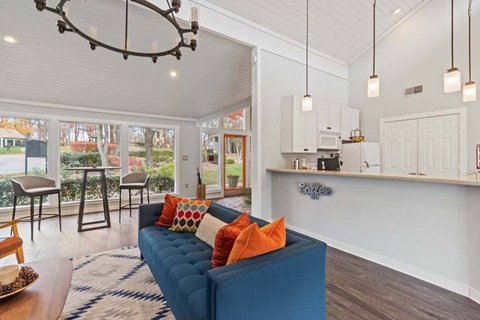 A blue couch with orange pillows sits in a living room with a kitchen in the background.