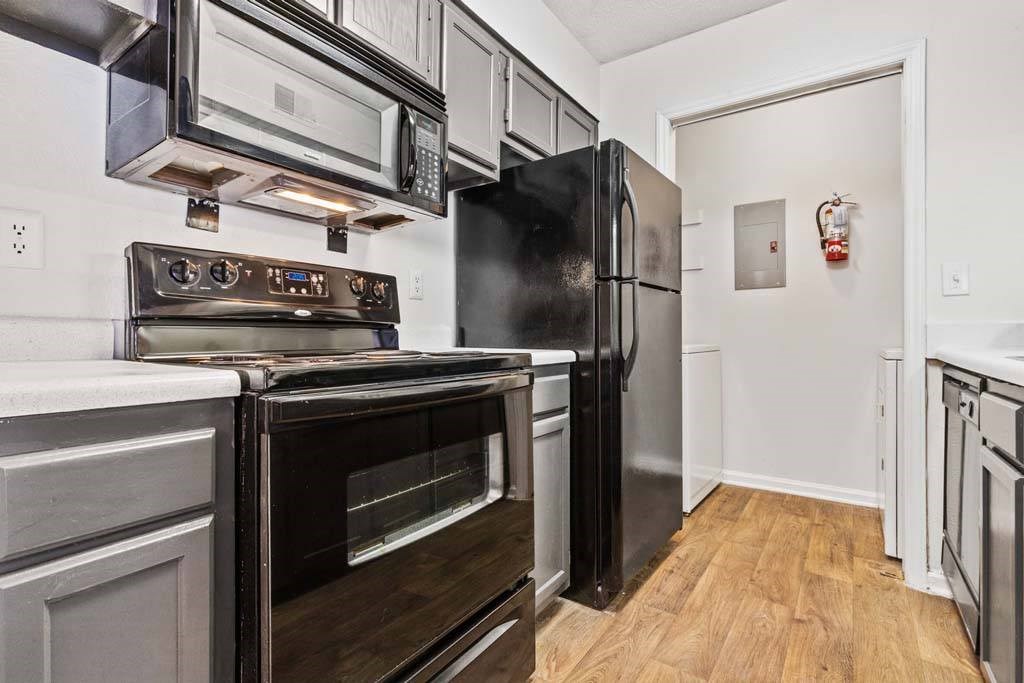 A black fridge and oven in a kitchen with wooden floors.