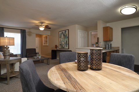 The Dining Room table is shown in the foreground with dark chairs surrounding and decor on the tabletop. The kitchen is shown on the right side with the Living Room in the background on the left.
