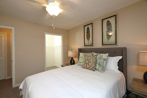 The Bedroom is a comfortable space with a large bed centered on the main wall. A large walk-in closet sits on the side of the room. The carpeted flooring continues throughout with furniture filling spaces around the room.