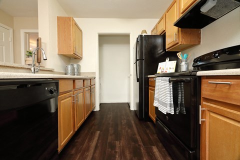 The B1 Kitchen has light oatmeal-colored countertops with light wood cabinetry. Black kitchen appliances contrast against the light paint. An open closet at the end of the galley-style room holds the full-size washer and dryer appliances.