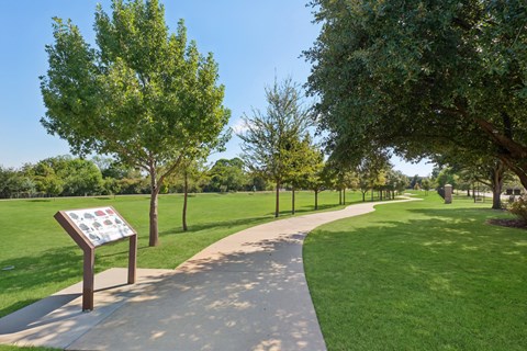 A sign in a park with a pathway and trees.