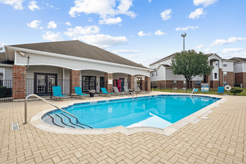 A swimming pool surrounded by a brick patio and a building in the background.