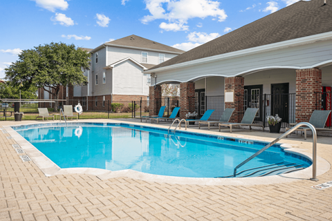 A swimming pool surrounded by a brick patio and a building in the background.