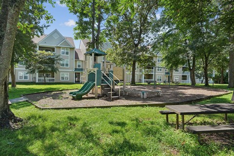 A playground with a green slide and picnic table in front of apartment buildings.