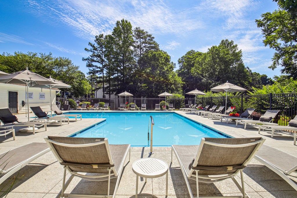A pool surrounded by chairs and trees.