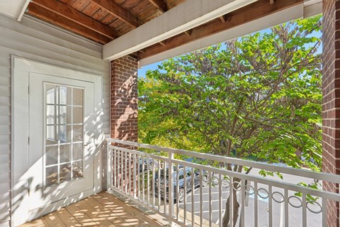 A balcony with a white railing and a view of a tree and a building.