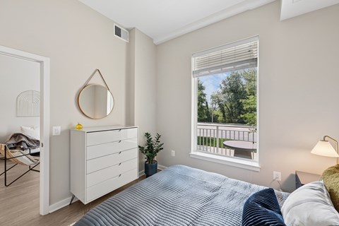 A bedroom with a bed, dresser, mirror, and window.