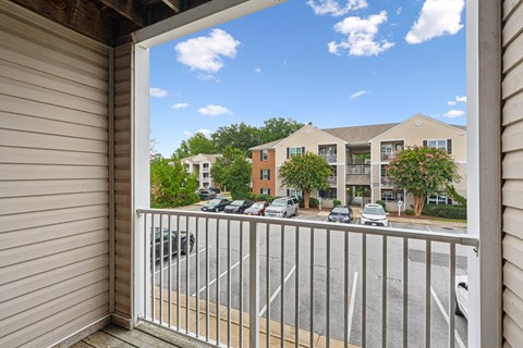 A view from a balcony looking out at a parking lot and apartment buildings.
