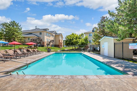 Outdoor swimming pool with lounge seating and shade umbrellas at Mayflower Harbor at Pilgrims Landing Apartments, Lehi, UT 84043