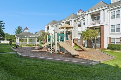 A playground with a slide and a gazebo in front of a building.