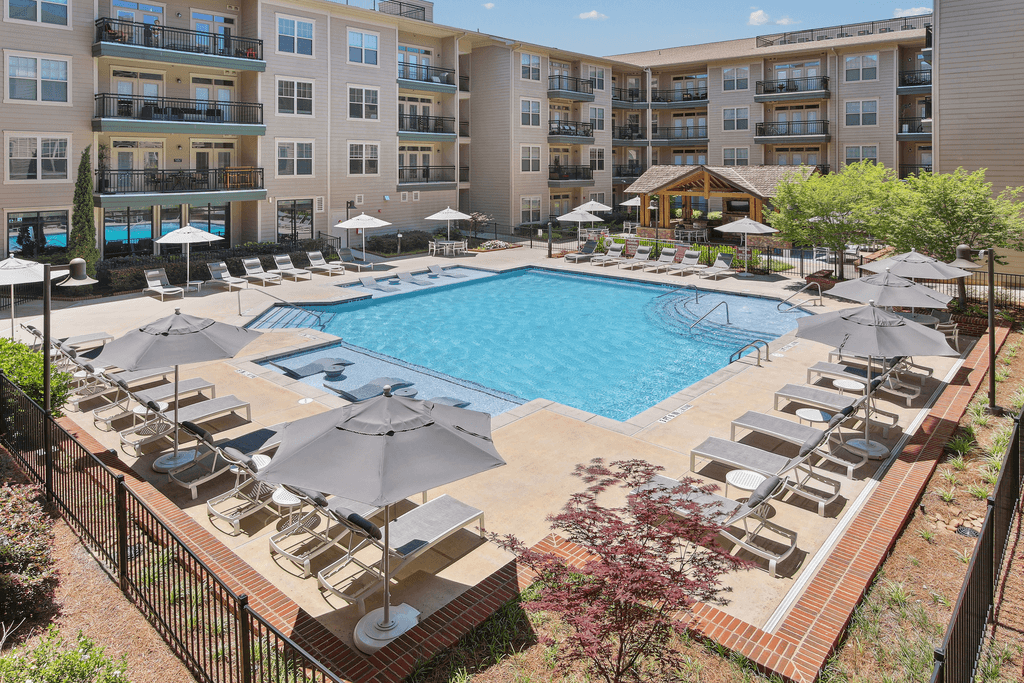 an aerial view of a pool with chairs and umbrellas and an apartment building