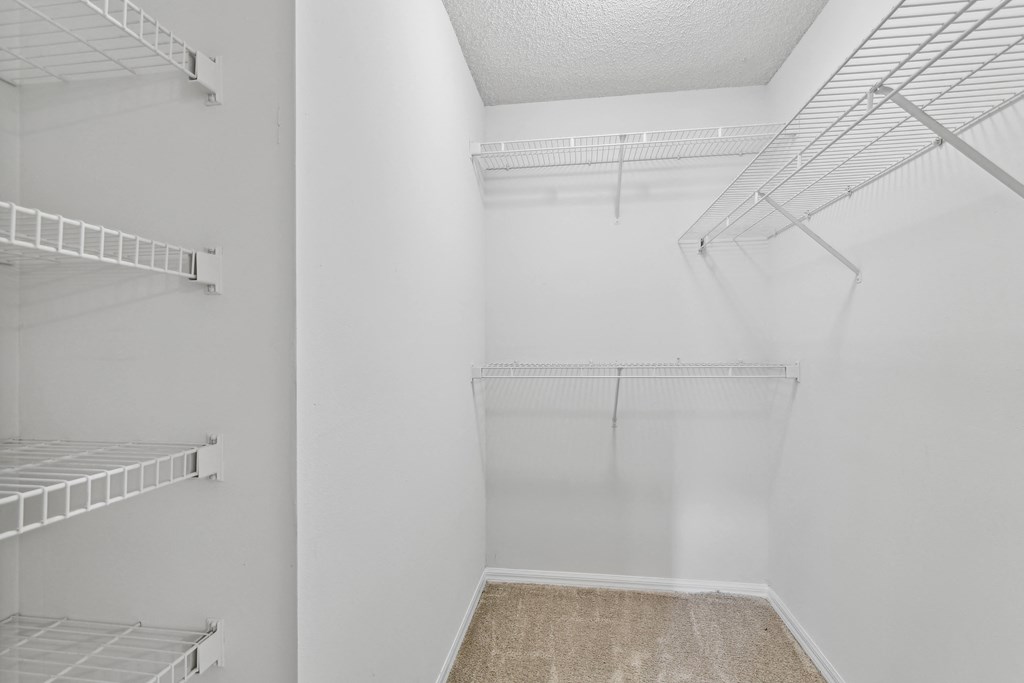 a spacious walk in closet in a white room with empty shelves