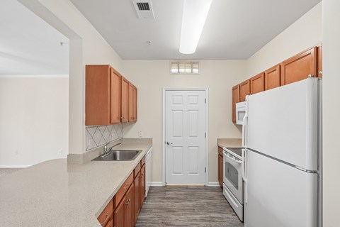 A kitchen with a white refrigerator, wooden cabinets, and a white door.