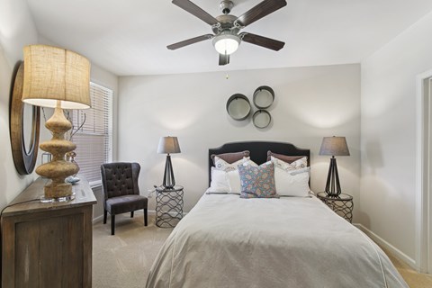 A bedroom with a bed, chair, and ceiling fan.