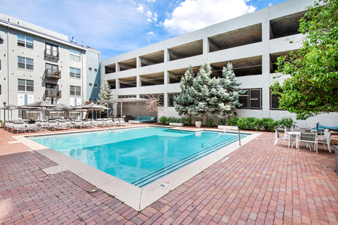 A pool surrounded by a brick patio and chairs.
