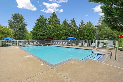 A large swimming pool surrounded by trees and chairs.