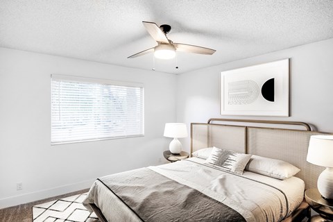 A bedroom with a bed, a ceiling fan, and a painting on the wall.