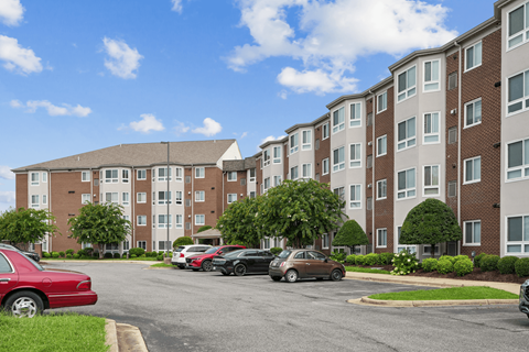 A red car is parked in a parking lot in front of a brick apartment building.