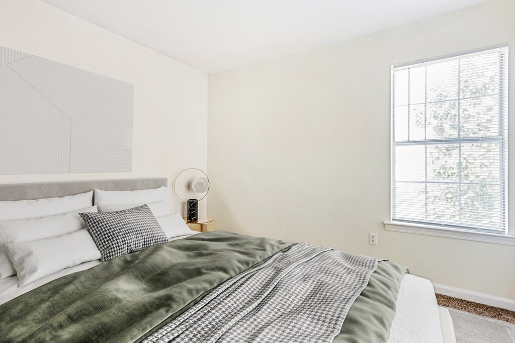 Staged bedroom with queen sized bed, art above bed, nightstand, and large windows in the background.