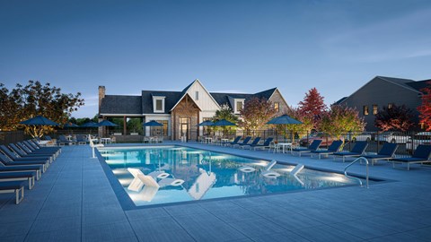 A large swimming pool surrounded by lounge chairs in front of a house.