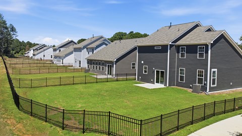 A black fence surrounds a grassy area with a house in the background.