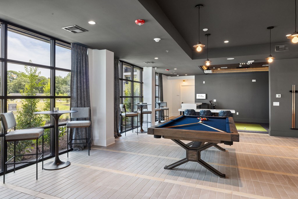 A pool table is in the middle of a room with a view of trees outside the window.