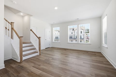 A spacious room with wooden floors and a staircase.
