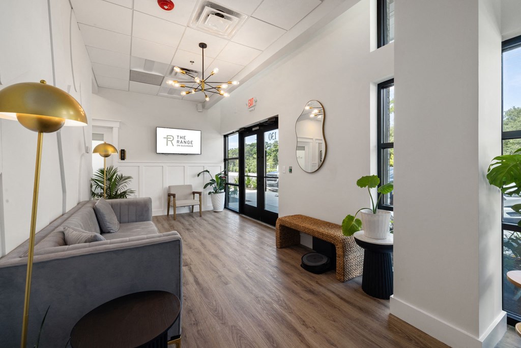 A well-lit waiting room with a grey couch, a yellow floor lamp, and a white wall with a mirror.