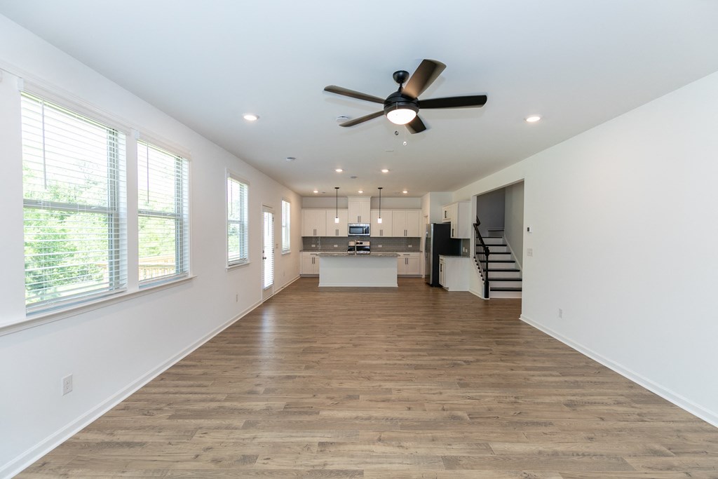a living room with a ceiling fan and a kitchen in the background