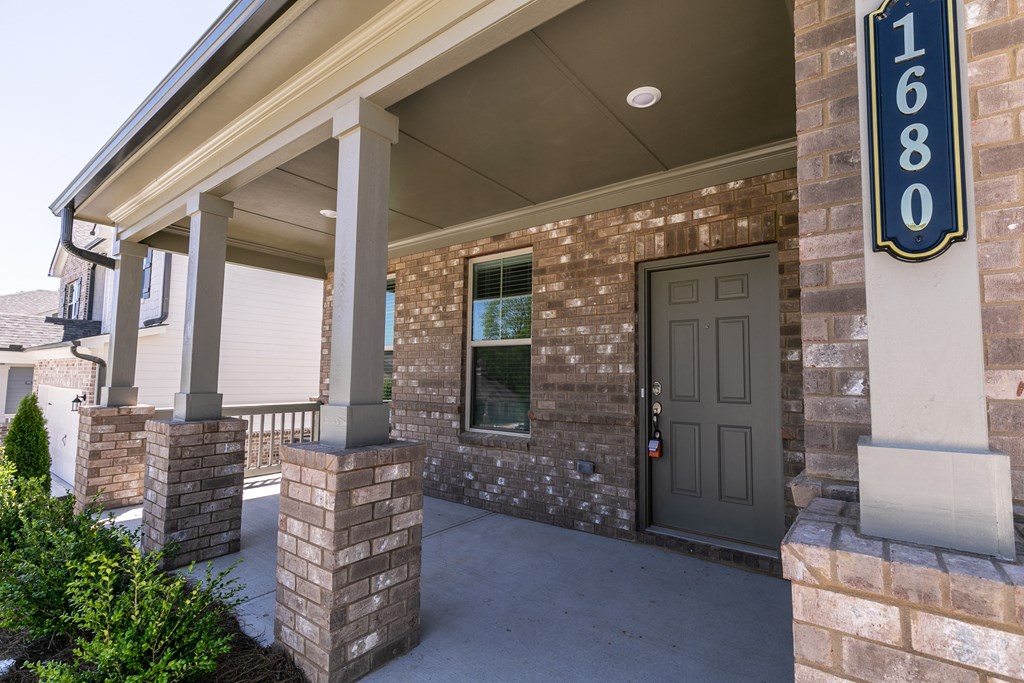 a front porch of a brick building with a gray door and a blue sign that reads 6
