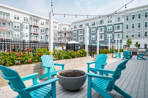 a patio with blue chairs and a fire pit and an apartment building