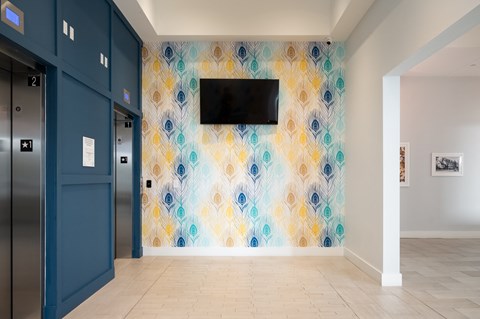 a hallway with blue doors and a colorful wall with a television on it
