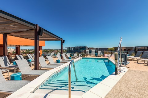 A swimming pool with lounge chairs and a covered area.