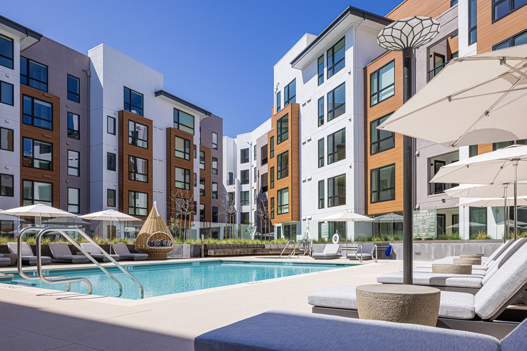 a swimming pool with chaise lounge chairs and umbrellas in front of an apartment building