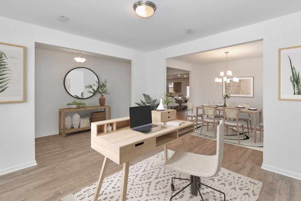 a living room with a laptop on a desk and a dining room in the background