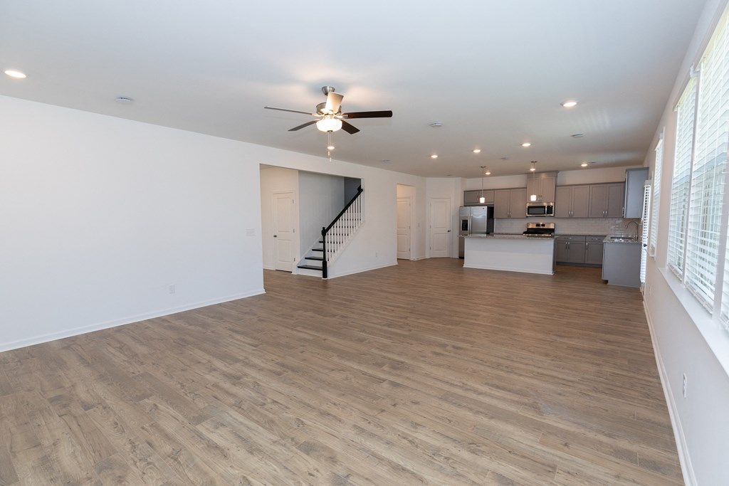 a living room with a ceiling fan and a kitchen in the background