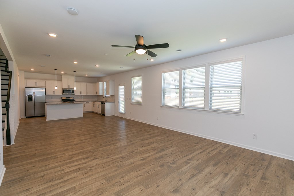 an empty living room with a ceiling fan and a kitchen in the background