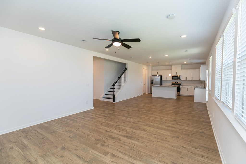 a living room with a ceiling fan and a kitchen in the background