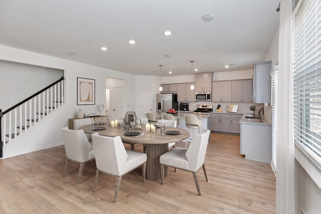 a living and dining room area with a kitchen in the background and a staircase in the foreground
