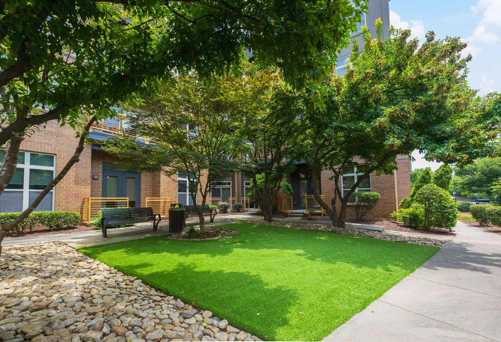 a green lawn in front of a brick building with trees and a bench