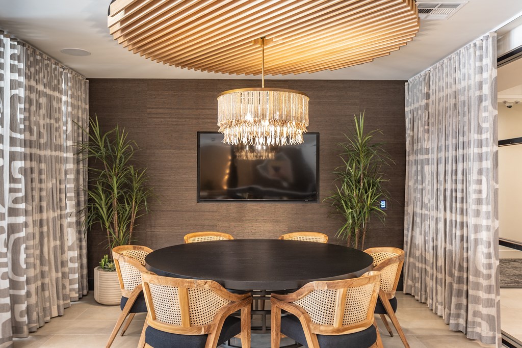 a round table with wicker chairs and a chandelier hangs above it