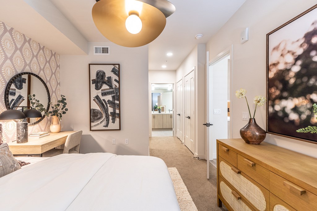a bedroom with a white bed and a wooden dresser with a vase of flowers on