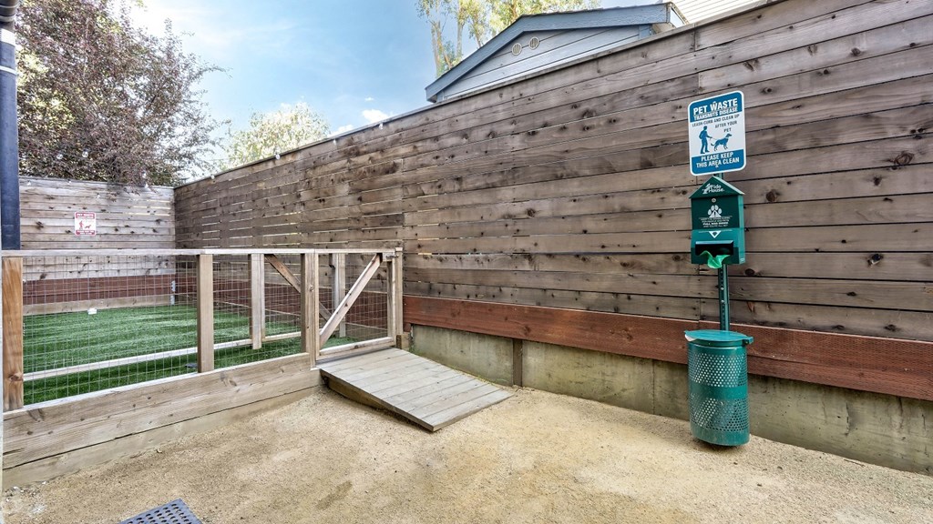 Fenced pet-friendly park with a designated waste disposal area, including a garbage can and waste bags for convenience.