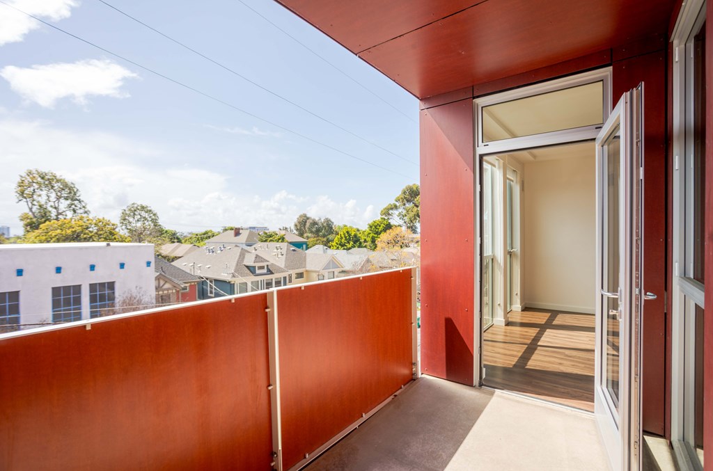 A balcony with a red wall and a glass door leading to a wooden deck.