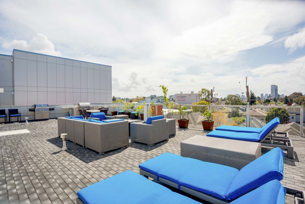 A rooftop patio with blue cushioned seating and a white wall.