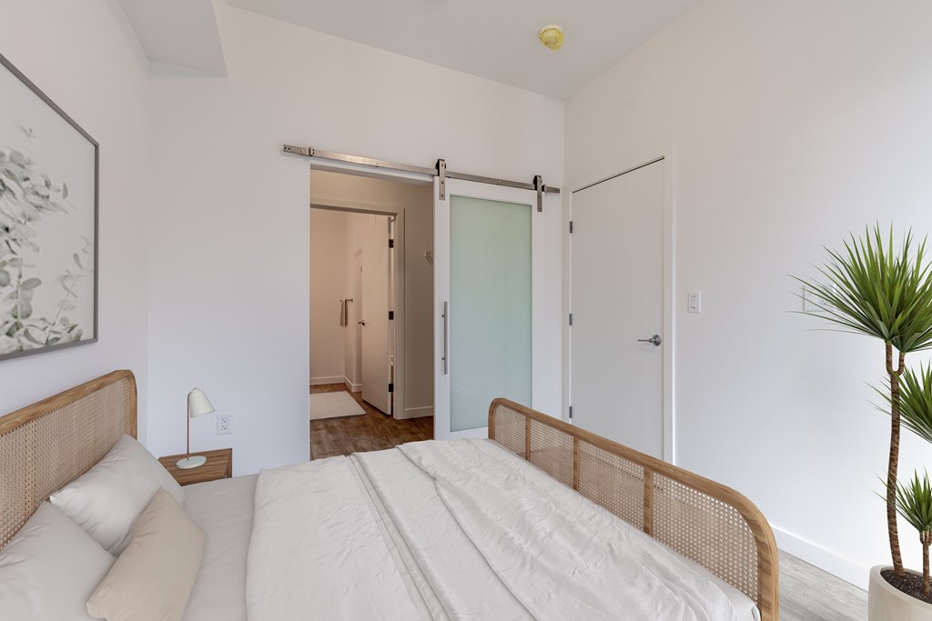 A bedroom with a bed, a plant, and a painting on the wall.