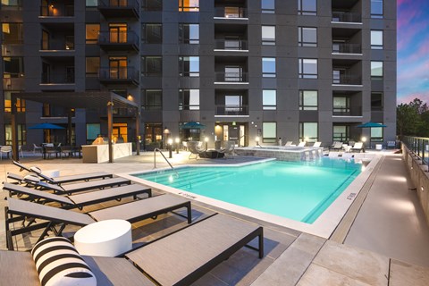 A large swimming pool with sun loungers and a striped bean bag in front of a large apartment block.